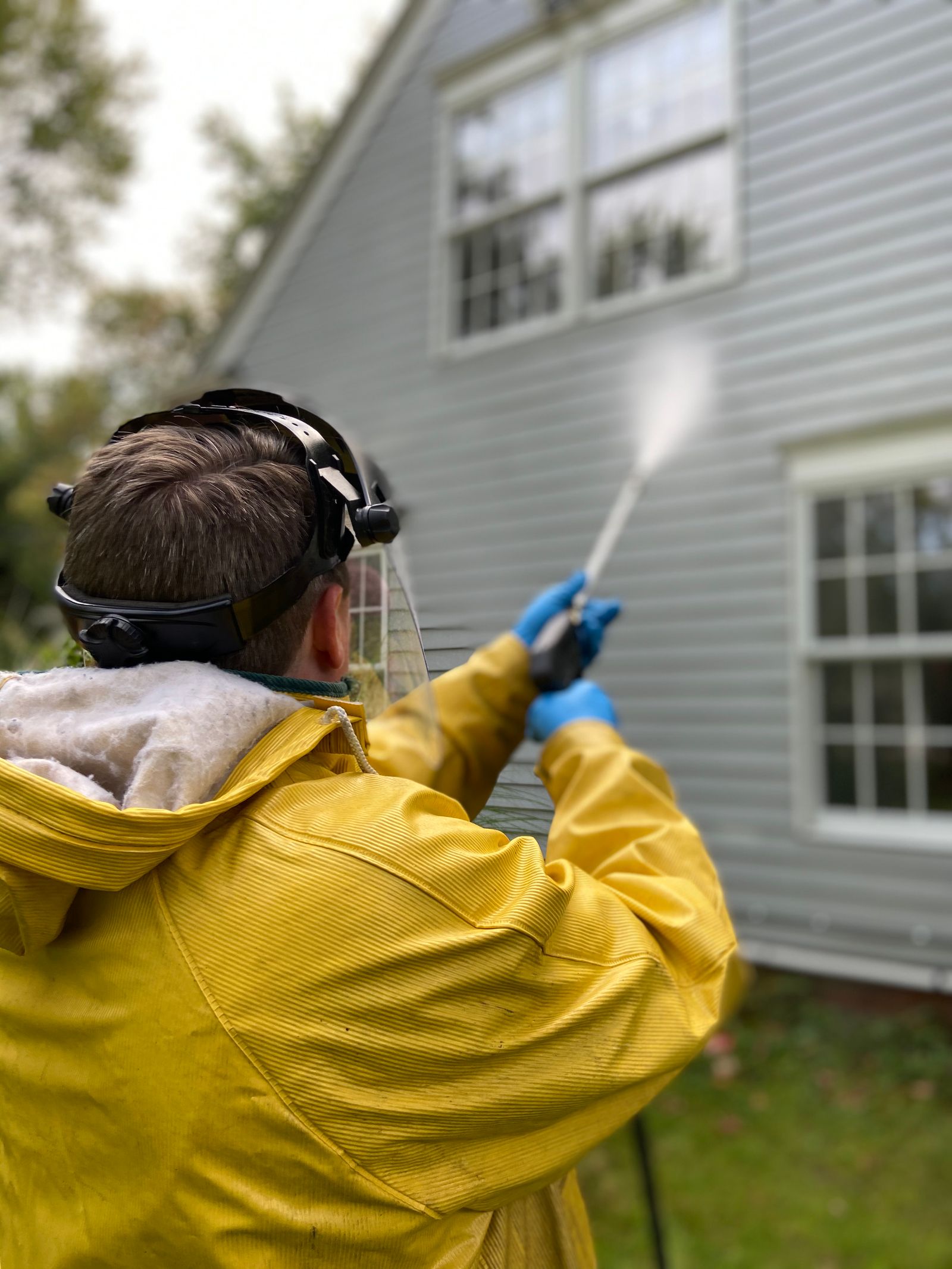 Pressure washing the side of a house in protective gear